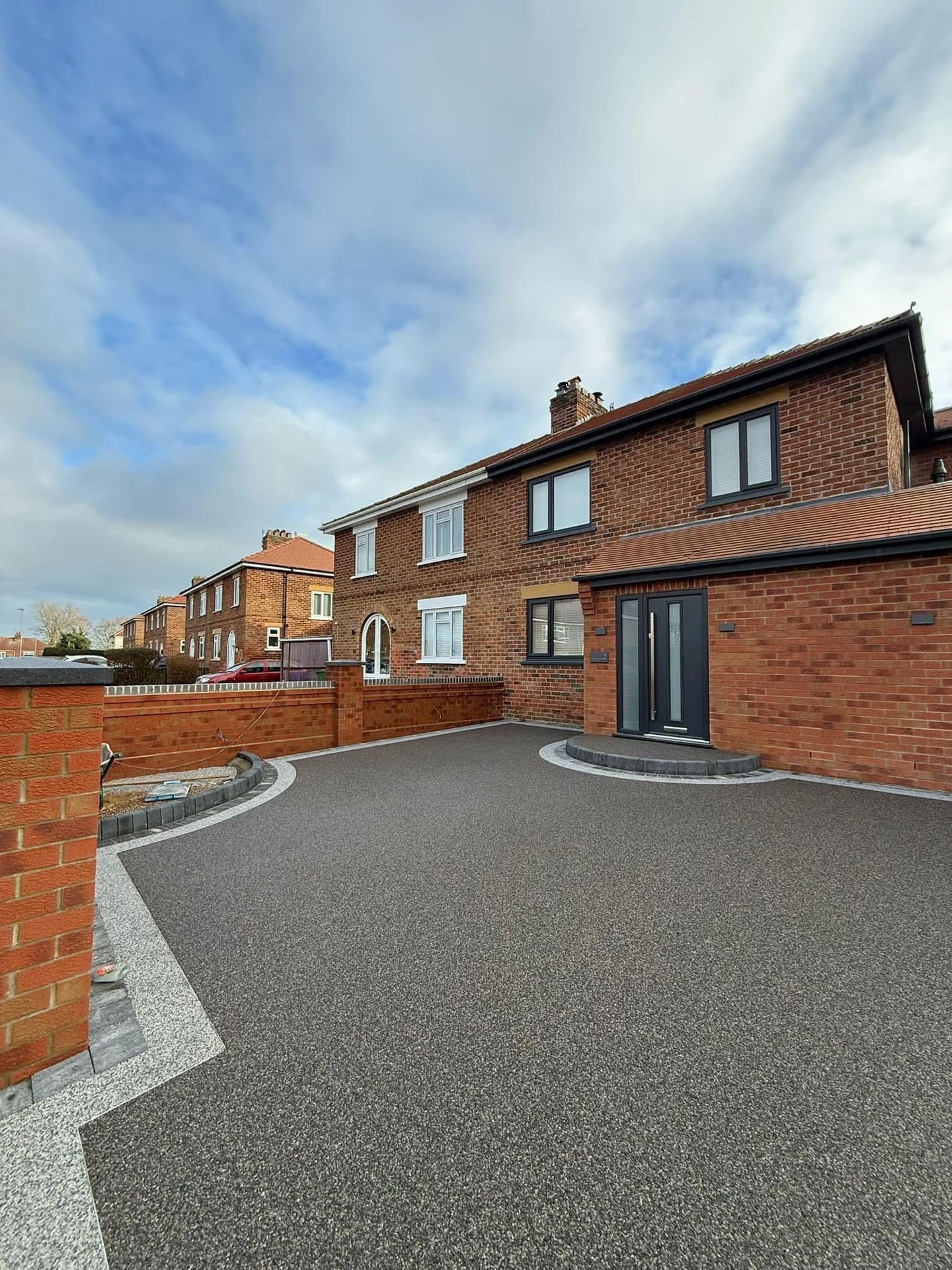 Brick house with a driveway and cloudy sky above.