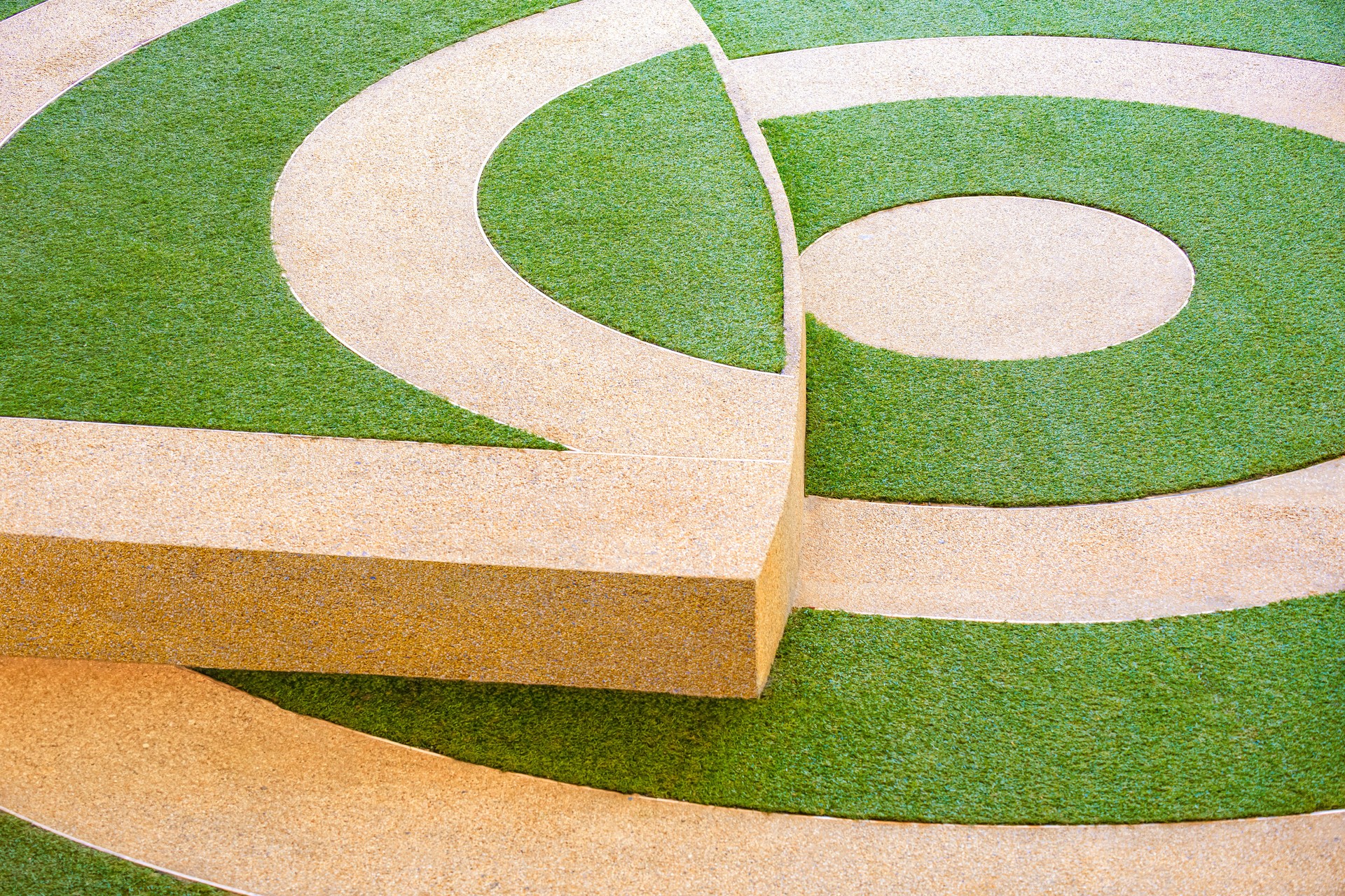 Geometric pattern of artificial green turf and exposed aggregate finish cobblestone in different level pavement floor at public park